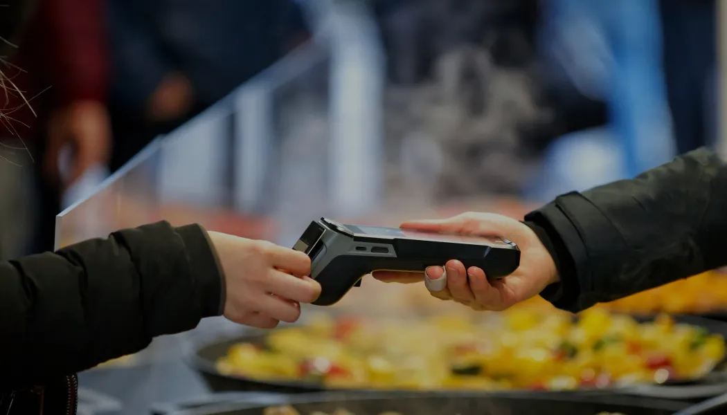 Pessoa usando cartão contactless em uma máquina de cobrança em um mercado.